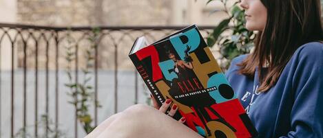 Una persona sentada en un banco al aire libre, sosteniendo un libro.