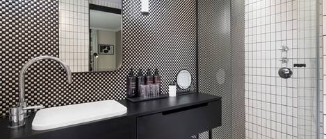 Un baño moderno con un salpicadero de azulejos a cuadros blanco y negro, un tocador negro con lavabo blanco y una mampara de ducha de vidrio.