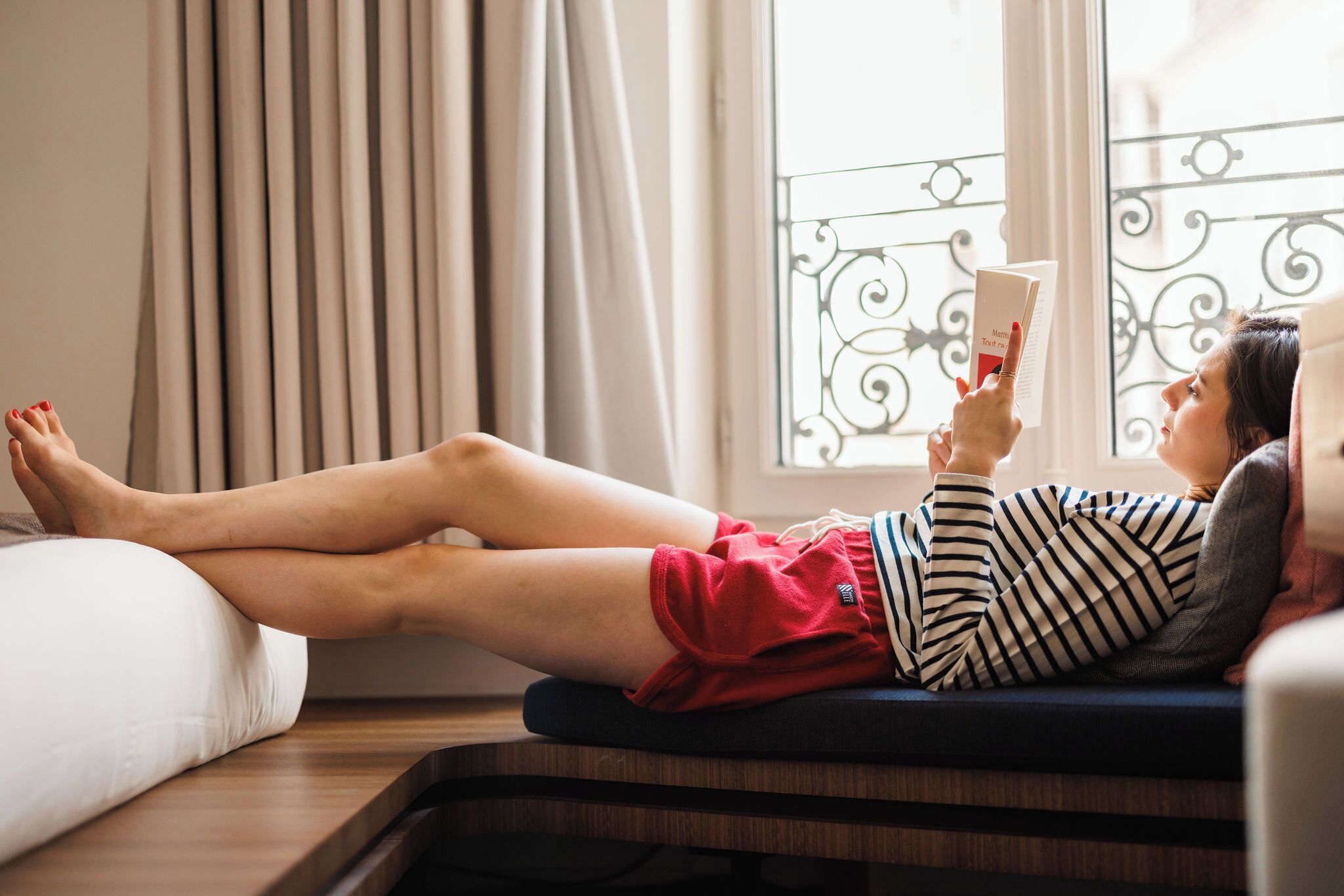 A person lying on a sofa with legs crossed, reading a book.