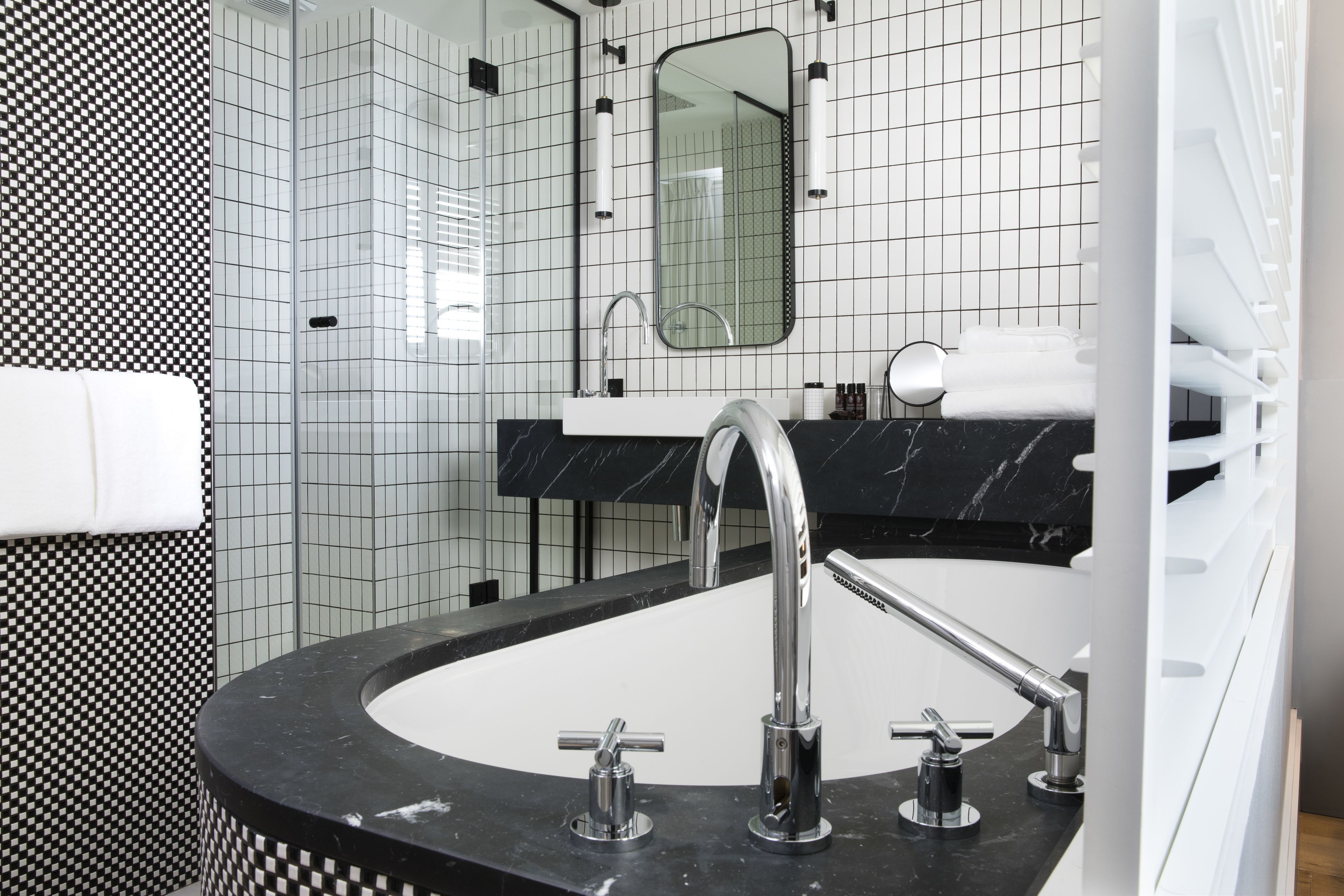Une salle de bain moderne avec un lavabo aux lignes courbes, un grand miroir et un mur recouvert de carreaux disposés en motif à carreaux.