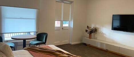 A hotel room with a bed, a round table, two chairs, a TV, and a window.