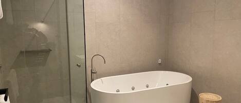 A modern bathroom with a freestanding bathtub, a glass shower enclosure, and a wooden bath mat.