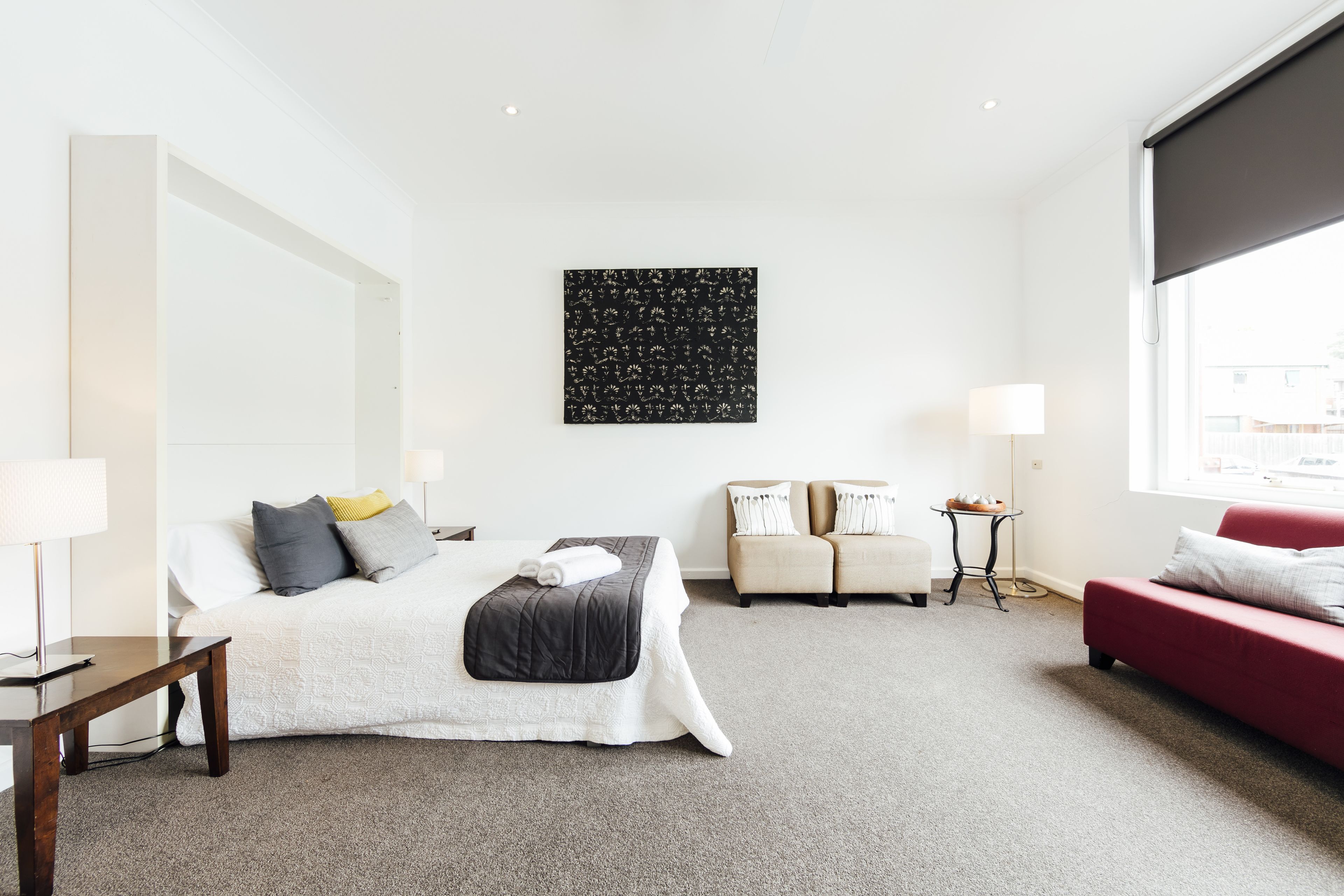 A hotel room with a bed, a red sofa, a small table, and a wall-mounted artwork.