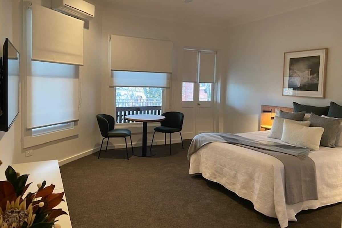 Un dormitorio con cama, escritorio, dos sillas, ventilador de techo y ventana con vista.