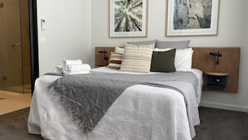 A neatly made bed with a grey quilt, a white towel, and several pillows. There are two framed artworks above the bed.