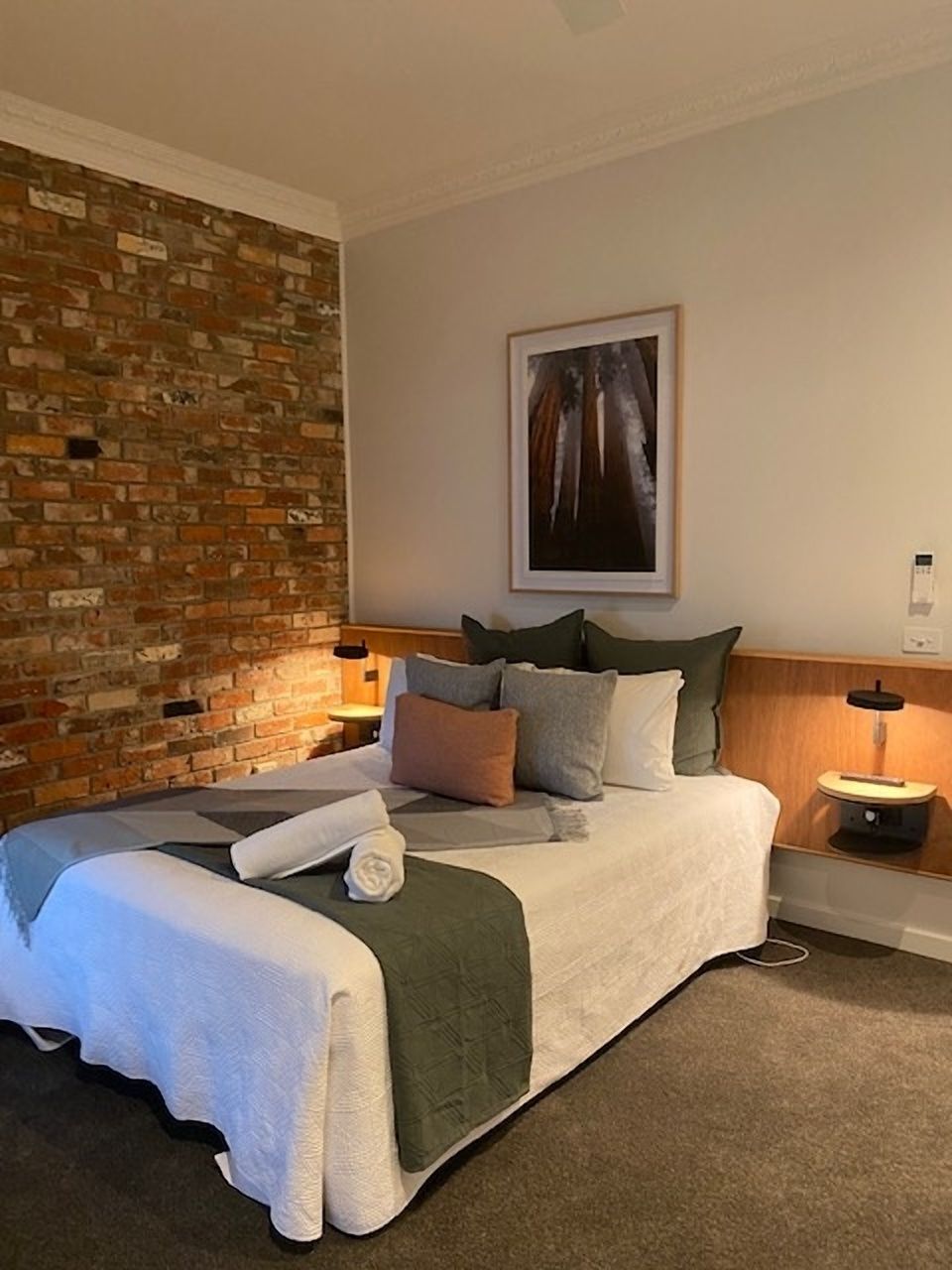 Een hotelkamer met een bakstenen muur, een bed met veel kussens, een ingelijste foto aan de wand en nachtlampjes.