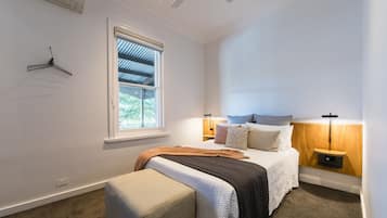 Un dormitorio con cama, mesitas de noche, una lámpara colgante, una ventana y un aire acondicionado instalado en la pared.