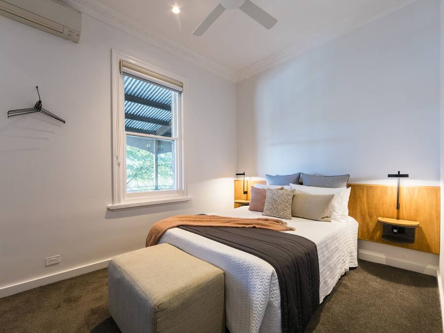 Un dormitorio con cama, mesitas de noche, una lámpara colgante, una ventana y un aire acondicionado instalado en la pared.