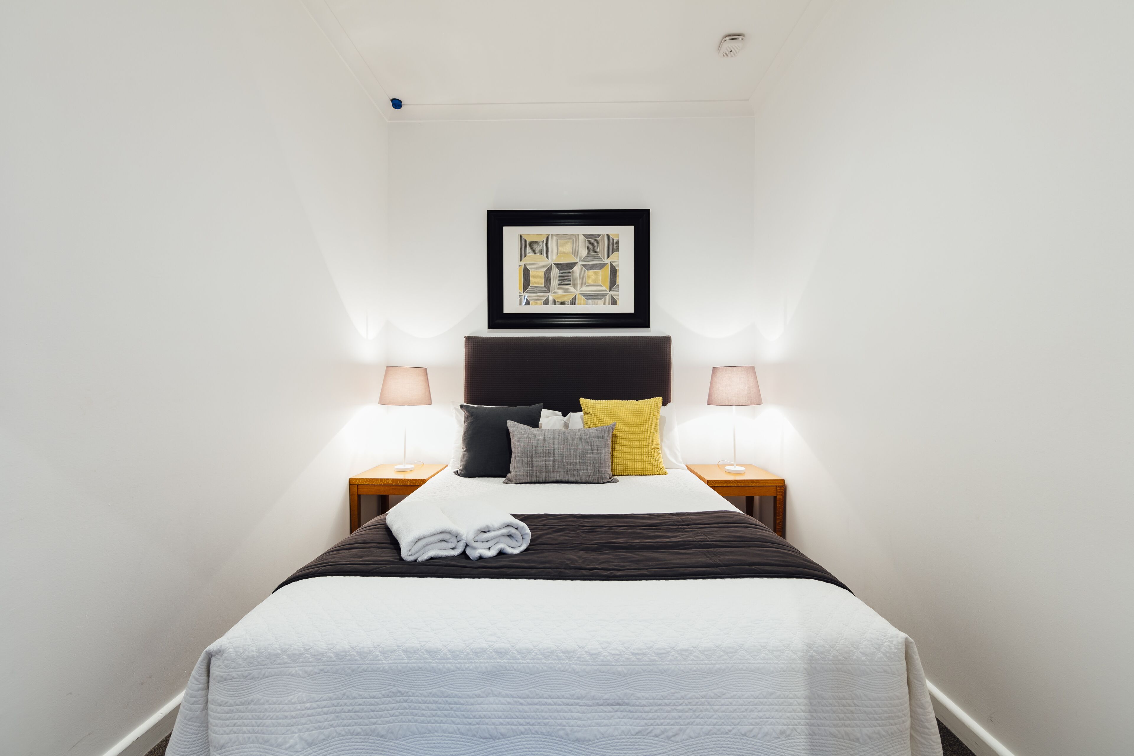 A neatly made bed with a black headboard, two bedside lamps, and a framed picture above the bed.
