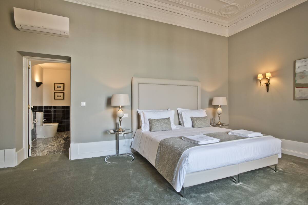 A bedroom with a large bed, two bedside lamps, a headboard, and a small side table.
