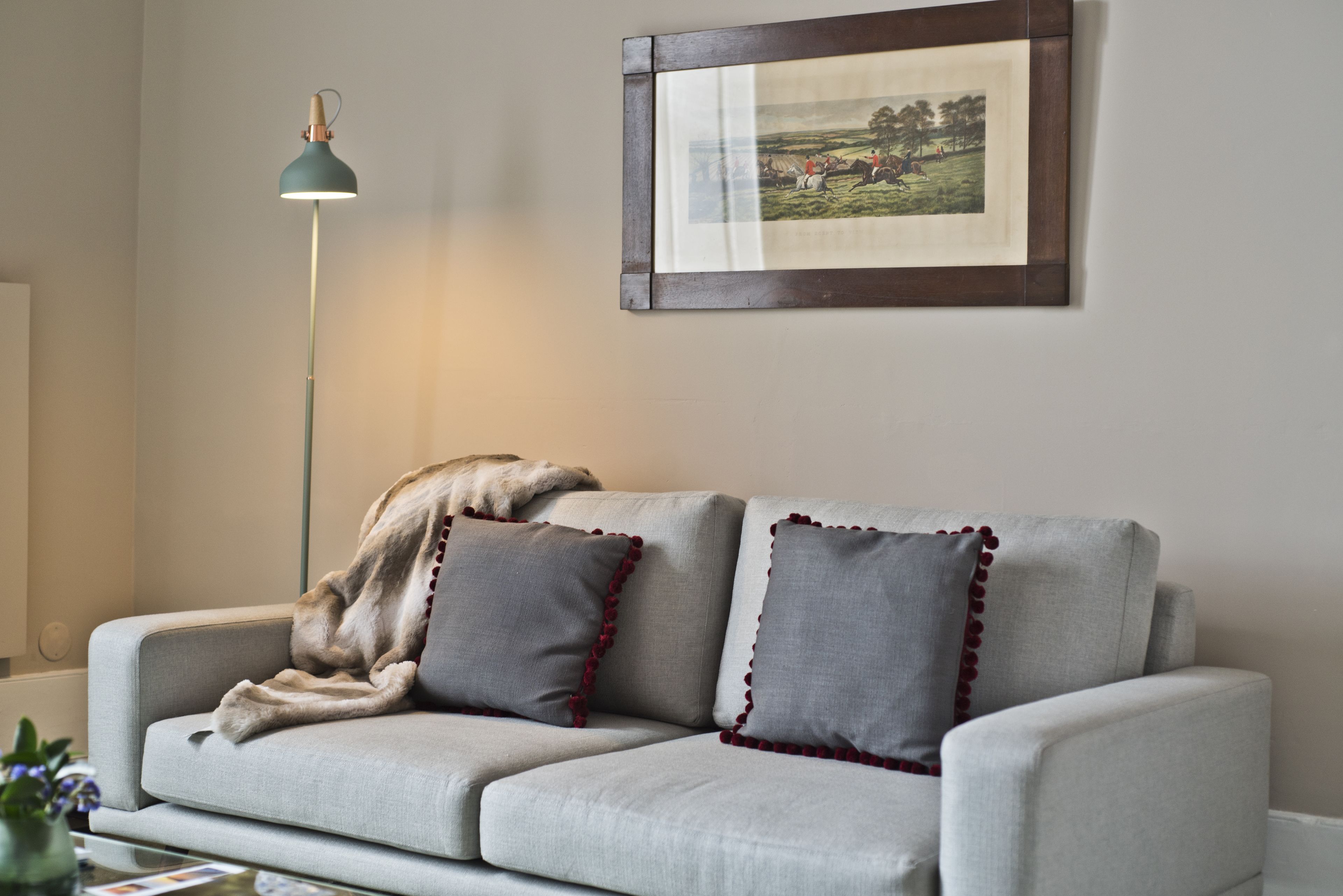 A modern living room with a grey sofa, a throw blanket, and a framed picture on the wall.