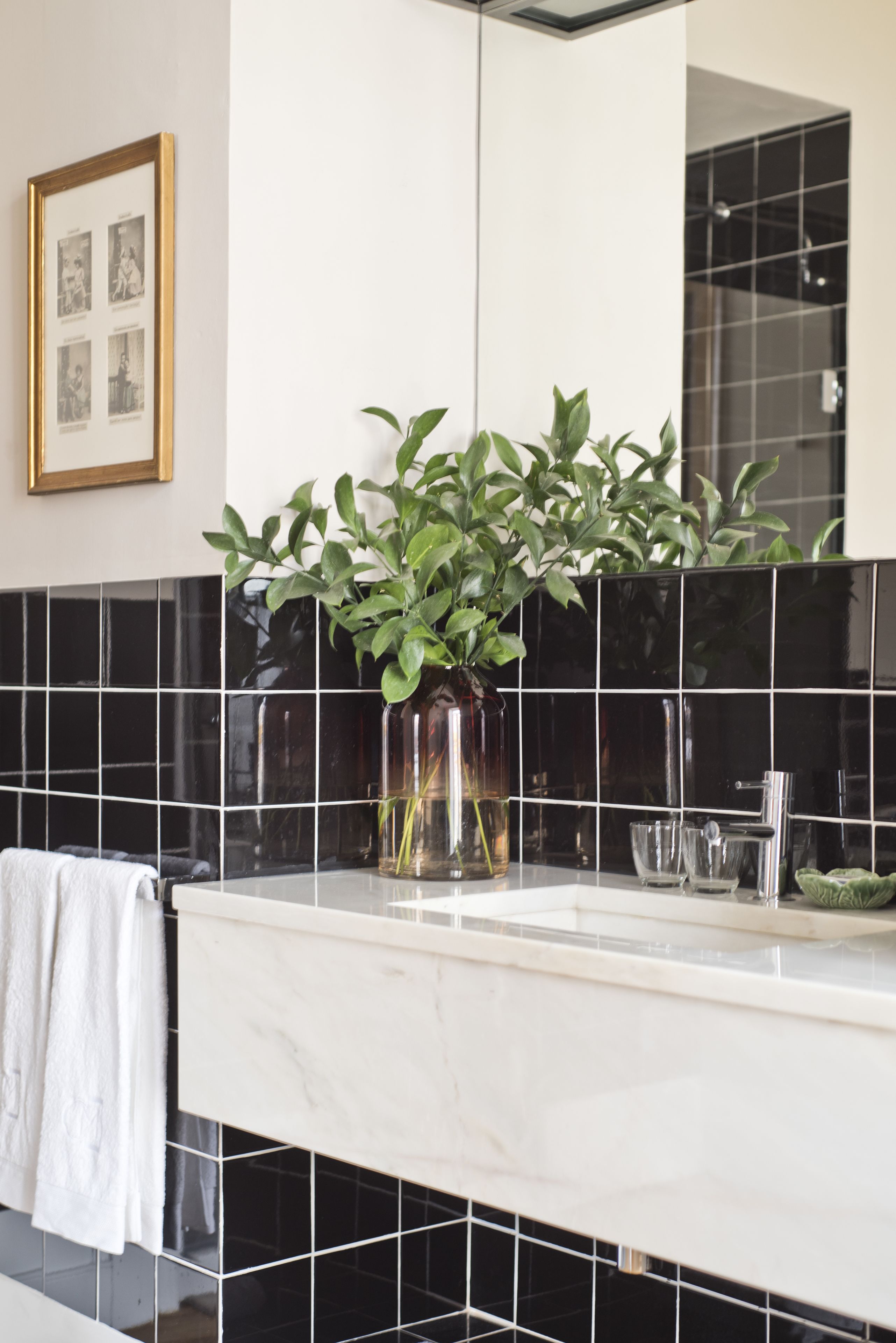 Un baño con lavamanos de mármol blanco, salpicadero de azulejos negros y una planta en maceta.