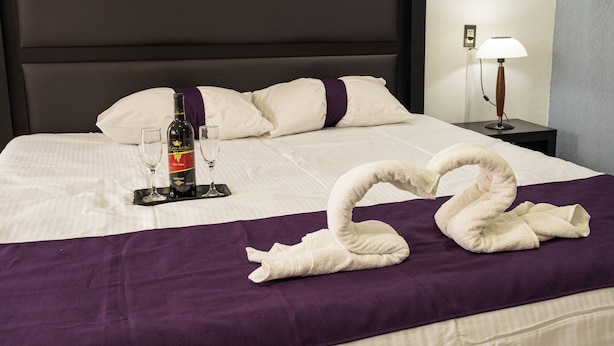 A neatly made bed with a purple blanket, a bottle of wine, and two wine glasses on a tray.