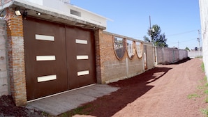 A gated building with two large brown doors, a concrete pathway, and a dirt road beside it.
