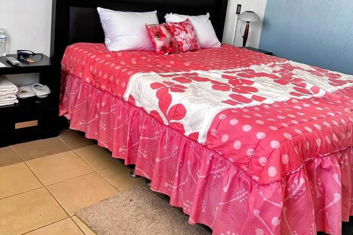 Une chambre à coucher avec une tête de lit noire, un lit recouvert d’une couvre-lit à motifs floraux rouges et blancs, des oreillers blancs, une table de chevet avec une lampe et un mur bleu.