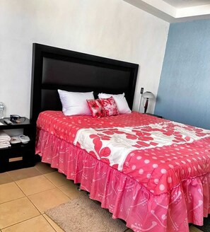A bedroom with a black headboard, a bed with a red and white floral bedspread, white pillows, a nightstand with a lamp, and a blue wall. - Hotel Boutique Tonalli (San Martin de las Pirámides)