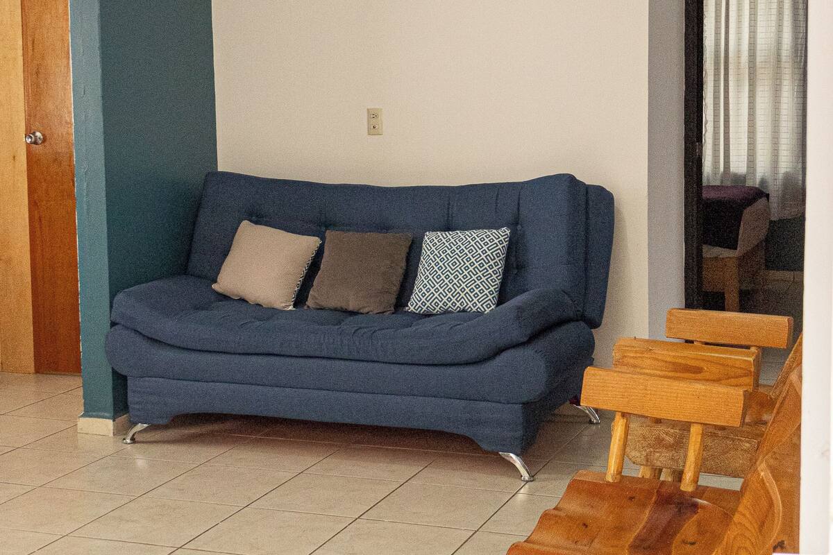 Un salon avec un canapé bleu, des bancs en bois et un sol carrelé.