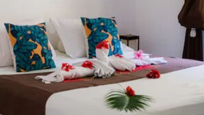 A hotel room with a neatly made bed, tropical-themed pillows, and a tropical-themed painting on the wall. - Bora Vaite Lodge (Bora Bora)