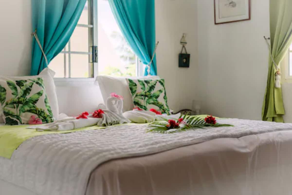 Una cama bien hecha con almohadones florales, un cabecero blanco y una manta verde.