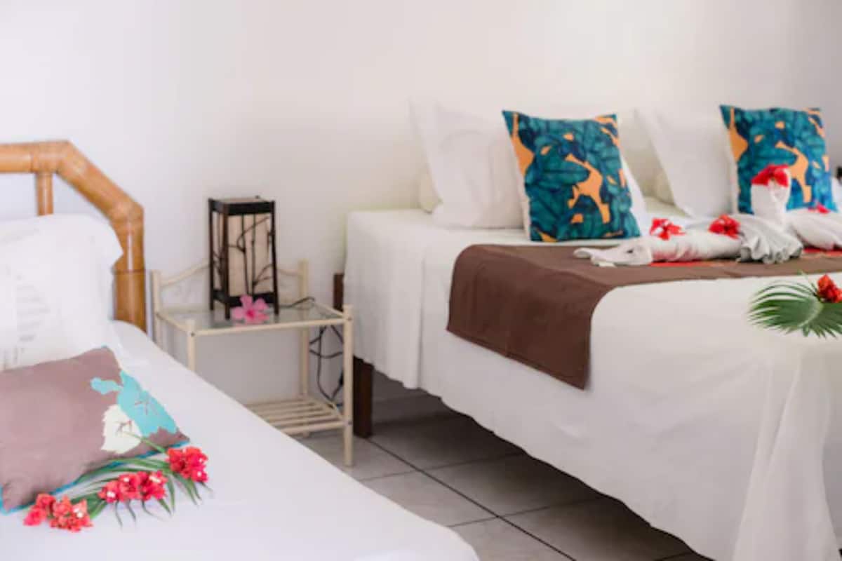 Una habitación de hotel con dos camas, ropa de cama blanca y almohadas decorativas.