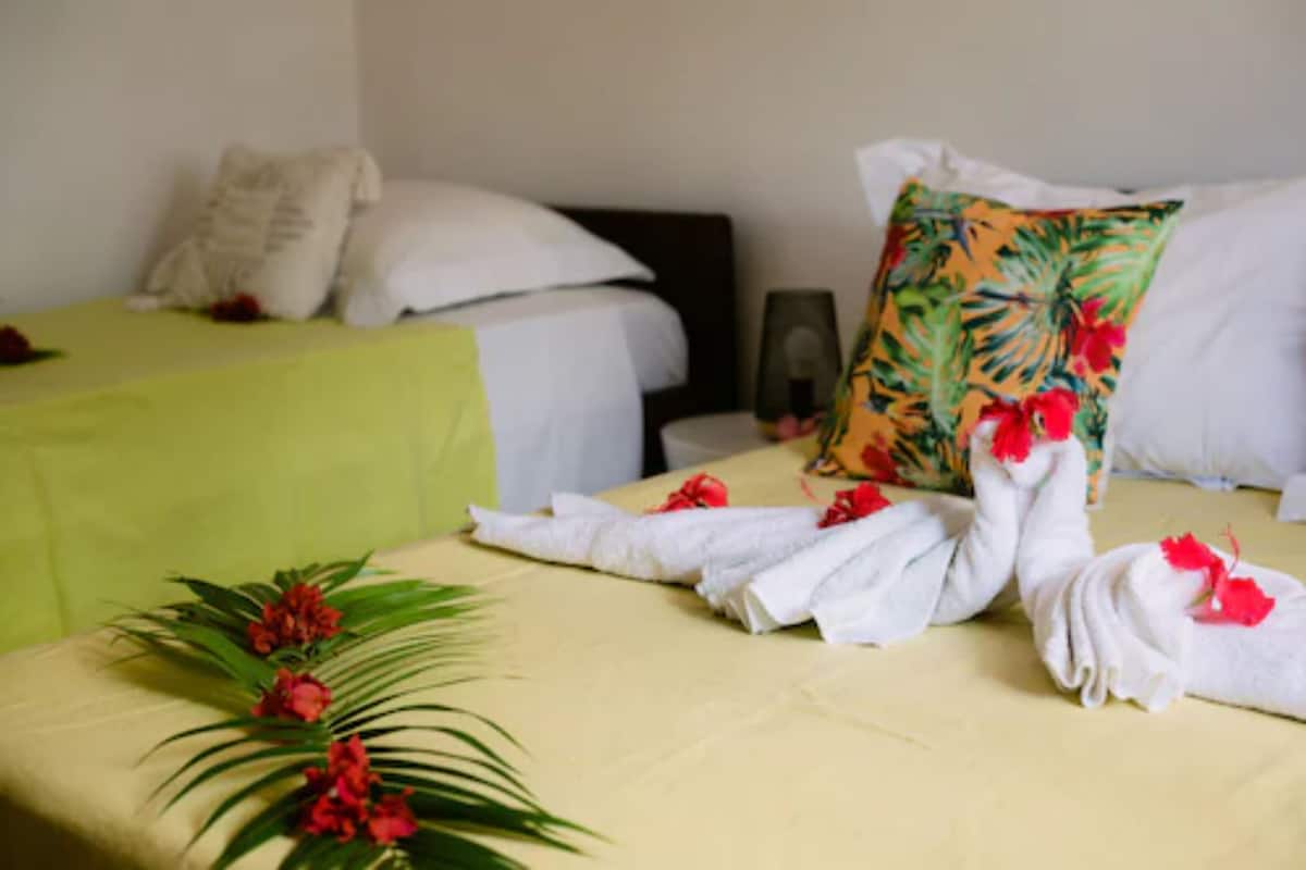 Habitación de hotel con dos camas, cada una con sábanas blancas y una colcha verde. Hay toallas decorativas con flores rojas sobre las camas.