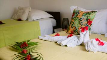 A hotel room with two beds, each with white linens and a green bedspread. There are decorative towels with red flowers on the beds.