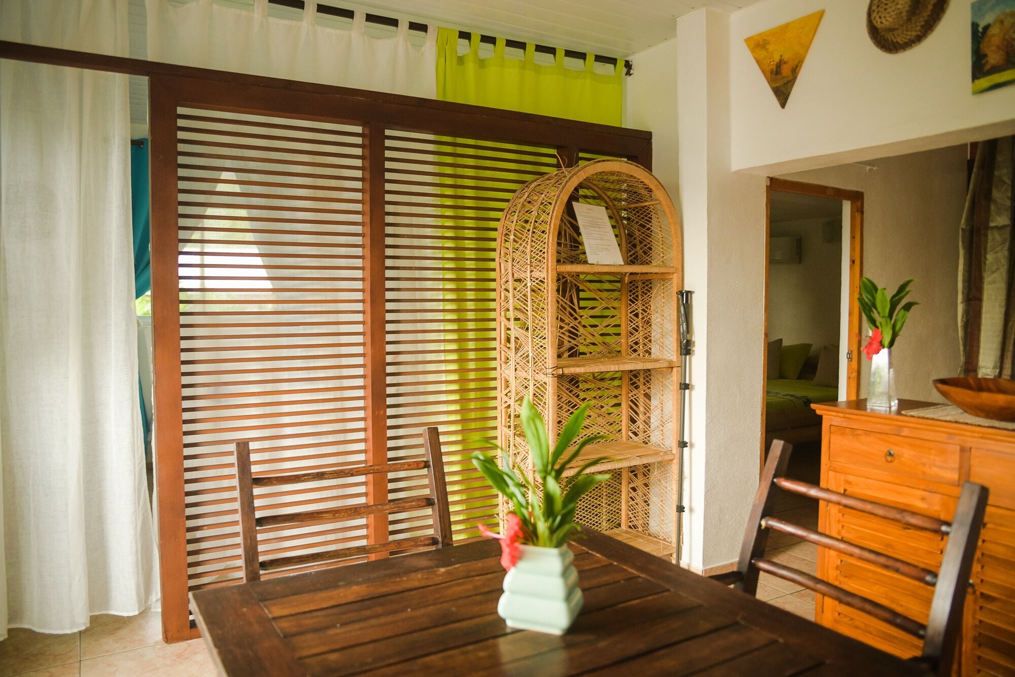 Un coin repas comprenant une table en bois, des chaises, une plante en pot, une étagère en osier et un meuble en bois.