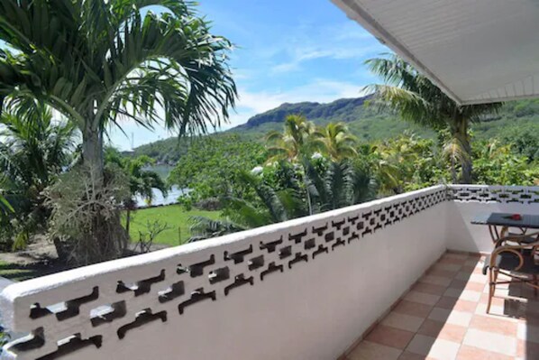 A balcony with a patterned wall, a table, and chairs, overlooking a lush landscape with palm trees and a mountain in the background. - Bora Vaite Lodge (Bora Bora)