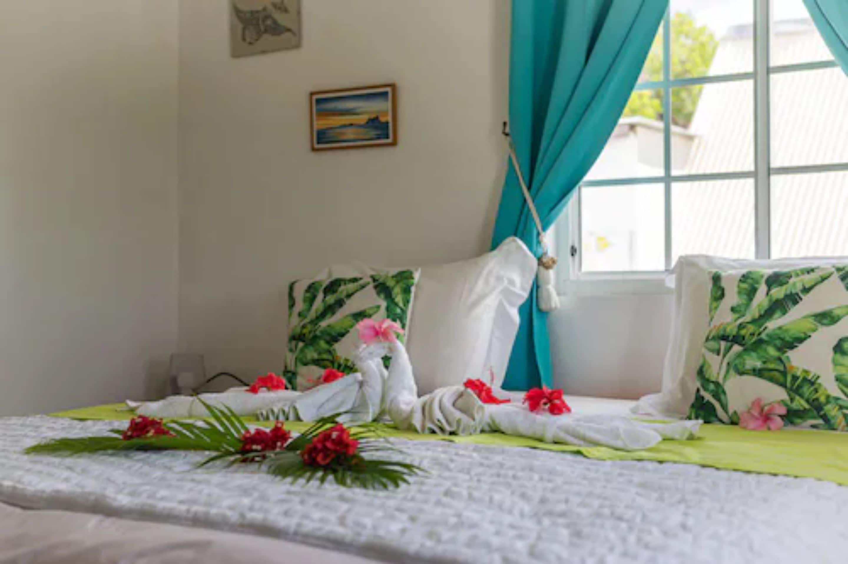 A hotel room with a bed, teal curtains, a painting on the wall, and a window with a view.