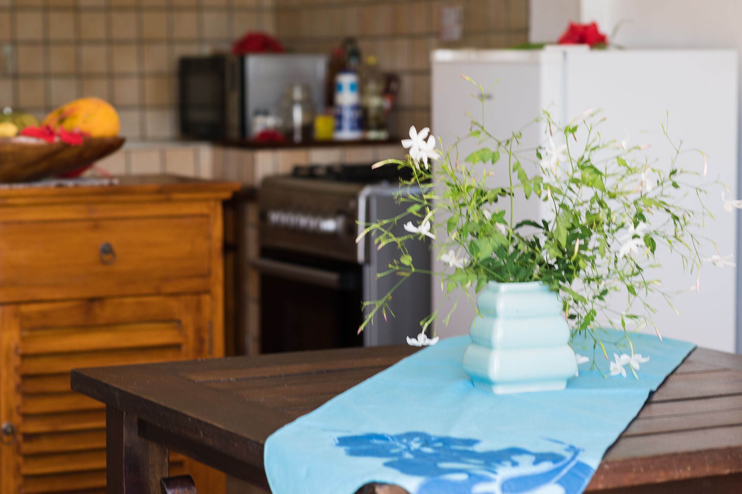 Une cuisine avec une table en bois, un vase rempli de fleurs et un panier de fruits.