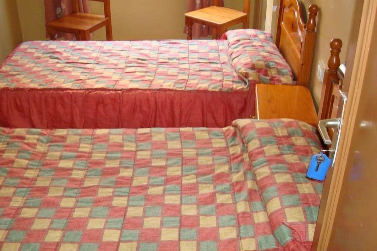 Une chambre avec deux lits, chacun recouvert d’une courtepointe à carreaux et agrémenté d’une jupe de lit rouge. On y trouve également une chaise en bois et une petite table.