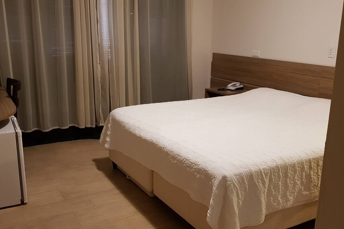 A hotel room with a bed, a small desk, a telephone, and a curtain.