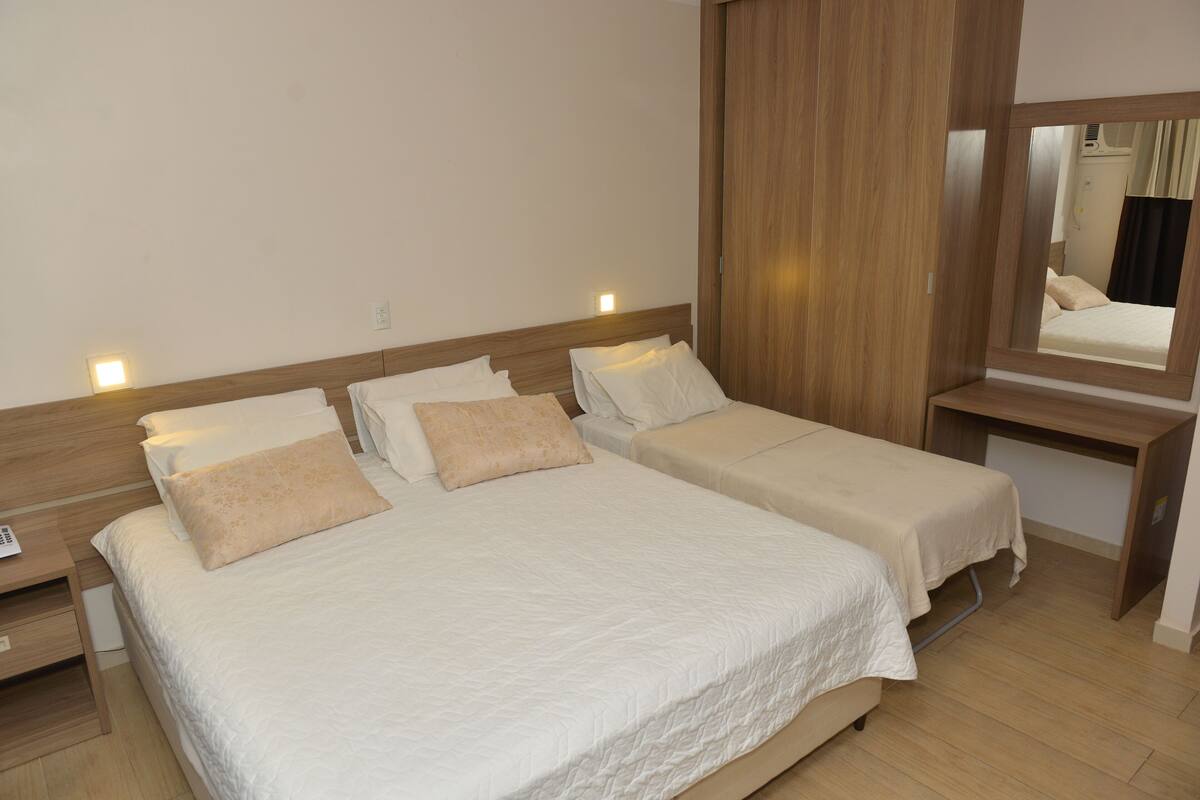 A double bed with a wooden headboard, a bedside table, and a mirror.