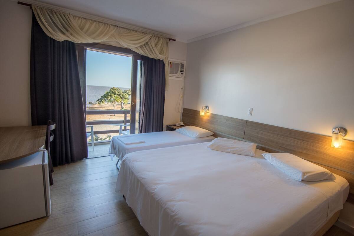 A hotel room with two beds, a desk, a chair, and a view of the beach.