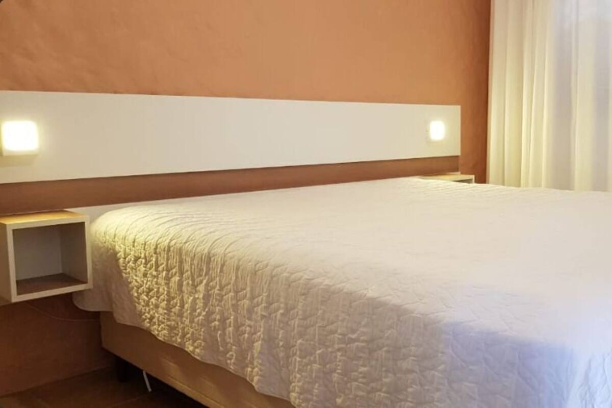 A hotel room with a large bed, a bedside table, and a headboard with built-in lighting.