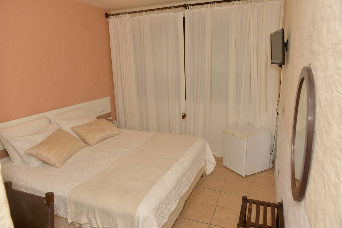 A bedroom with a bed, a small bedside table, a TV mounted on the wall, and a mirror.