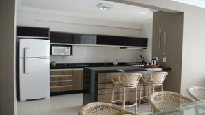 A modern kitchen with a refrigerator, microwave, and stove. There are wicker chairs and a glass table. - Nice apartment, right on the beach and in a great location. (Meia Praia Itapema)