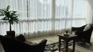 A room with a large window, a potted plant, two wicker chairs, a small table, and a patterned rug. - Nice apartment, right on the beach and in a great location. (Meia Praia Itapema)