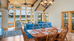 A spacious dining area with a wooden table and chairs, large windows, and a ceiling fan. - Stoney Point by Seaside Vacations & Sales (Chincoteague Island)