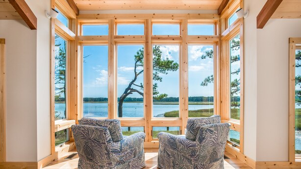 A room with large windows, wooden beams, and two patterned chairs. - Stoney Point by Seaside Vacations & Sales (Chincoteague Island)