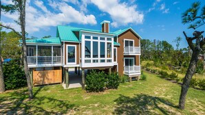 A two-story house with a green roof, large windows, and a balcony. - Stoney Point by Seaside Vacations & Sales (Chincoteague Island)