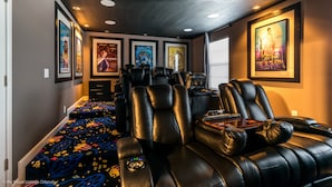 A home theater room with black leather reclining chairs, a carpet with colorful patterns, and framed movie posters on the walls. - 1574 Observer Lane (Davenport)