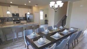 A modern kitchen with stainless steel appliances, a dining area with a long table set for six, and a staircase leading to another level. - 1541 Mulligan Blvd (Davenport)