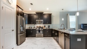 A modern kitchen with dark cabinetry, stainless steel appliances, and a marble floor.