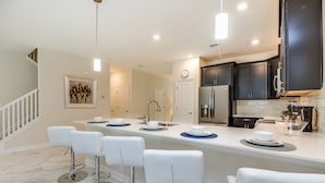 A modern kitchen with dark cabinets, a white countertop, and a bar area with white stools.
