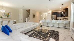 A modern living room with a white sectional sofa, a glass coffee table, and a staircase leading to the upper floor.