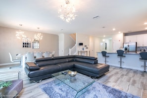 Ein modernes Wohnzimmer mit einem Ecksofa, einem Glastisch und einer Chandelier.