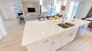 Une cuisine moderne dotée d’un grand îlot central, de meubles blancs et d’un évier à deux bacs.