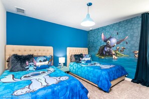 A bedroom with two beds, blue bedding, and a wall mural of Stitch from Lilo & Stitch.