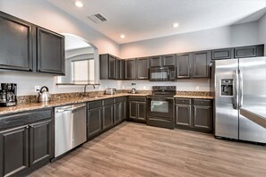 Una cocina moderna con armarios oscuros, electrodomésticos de acero inoxidable, encimeras de granito y piso de madera.